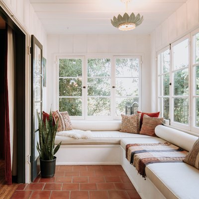A sunroom with a white bench seating and a snake plant on a brick floor