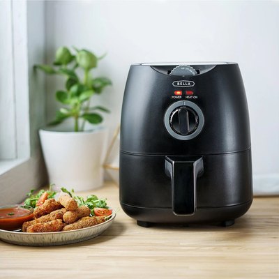 A black air fryer next to a plate of fried food on a table