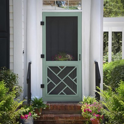 A green screen door on a white house with a brick porch