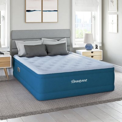 An air mattress next to a bed frame with a stack of pillows on top of it