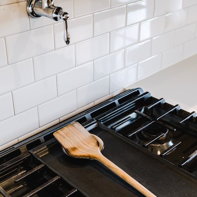Stovetop with a wood utensil on a holder and a white tile backsplash with a pot filler faucet