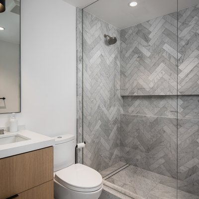 A large glass shower with herringbone tile and recessed lighting in the ceiling