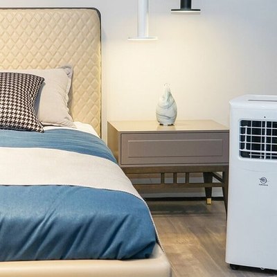 White portable air conditioner in beige and white bedroom with blue and white bed linens and black accents