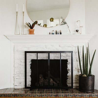 Large white brick fireplace with screen and large round mirror hanging above