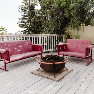 Red metal couches around fire pit on large white deck