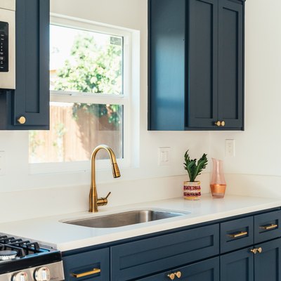 Kitchen with dark cabinets with gold handles and white countertop with single-handle kitchen faucet and a houseplant
