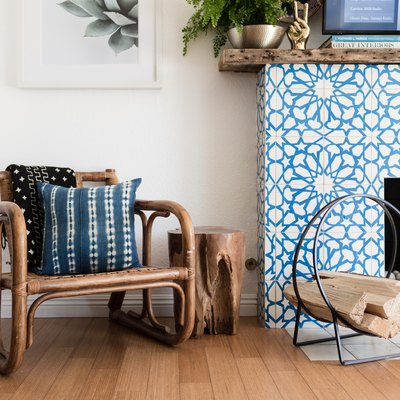 Boho chair, with a Shibori pillow, black-white patterned blanket, and a Moroccan star tile, wood mantel fireplace.
