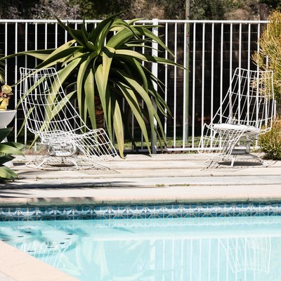 Swimming pool with Modernist style wire chairs, white drum side tables, and outdoor plants.