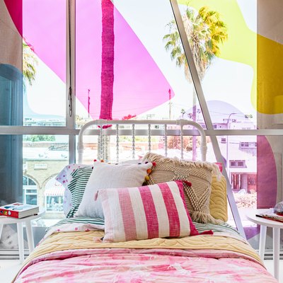 Pink and yellow themed kid's room with colorful bedding, throw pillows, and white furniture