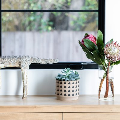 A wood sideboard with a sculpture, plant in a vase and vase of pink flowers
