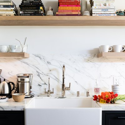 White calcutta wall of a kitchen with white sink and wood shelving with books