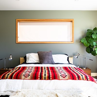 A bedroom with a large plant, wood framed windows and white-green walls