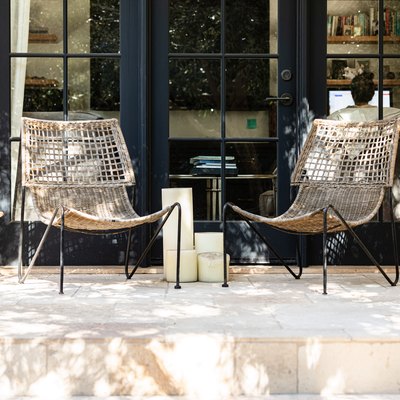 Three wicker patio chairs on a front porch by black framed windows.