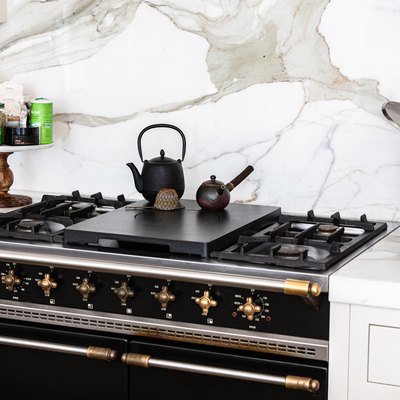 Stovetop with teapots in a kitchen with white countertops and granite backsplash