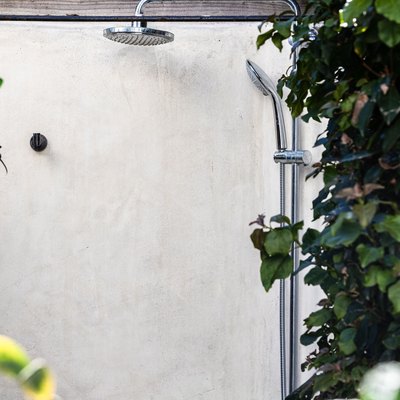 An outdoor shower by a white wall surrounded by ivy