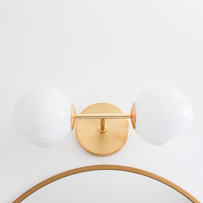 Gold wall sconce with globes over a mirror
