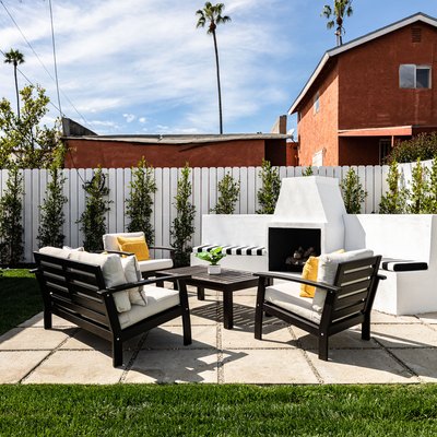 Paver patio with an outdoor fireplace, patio chairs and table surrounded by a white face lined with green trees