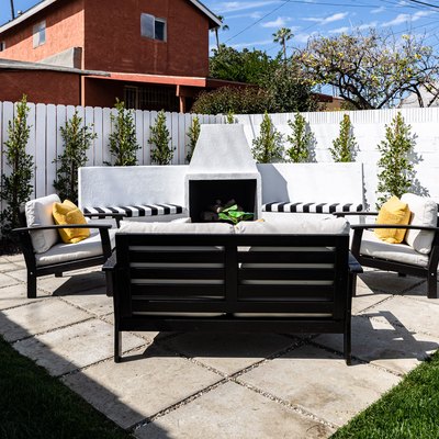 a paver patio with black and white outdoor patio chairs, a white privacy fence with evenly spaced small green trees