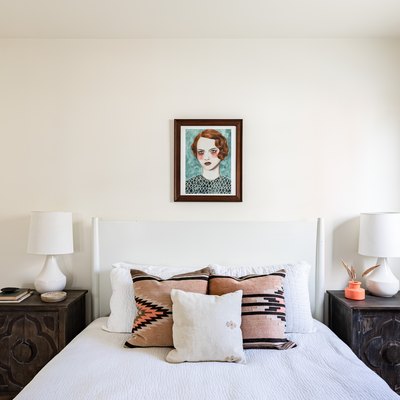 white bedroom white white bed, painting of red-haired woman, and dark wood nightstands