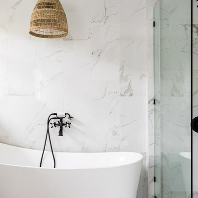 A minimalist bathroom with a bathtub, glass door shower and wicker light fixture