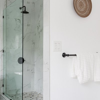 A glass shower in a white walled bathroom with a woven plate wall hanging