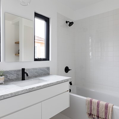 White tiled bathroom with bathtub, black shower head and faucet, black-framed windows, and marble countertop