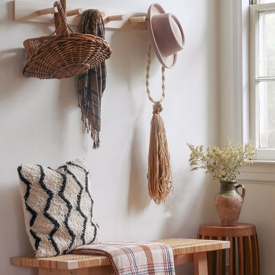 Wood peg board with a basket, scarf, and hat over a wood bench in a hallway