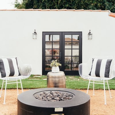 California-modern style backyard space with black fire pit, two white chairs, black and white pillows, and a metallic side table.