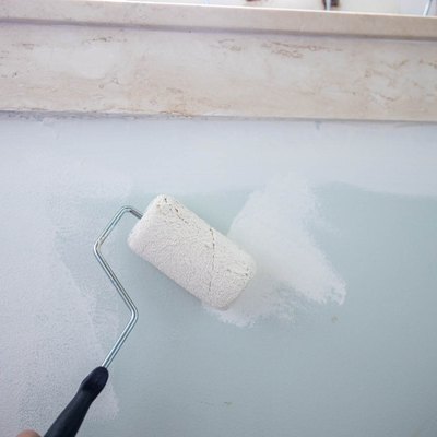 Paint roller with white paint, painting over a light blue wall
