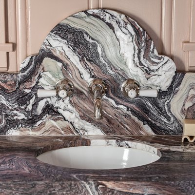 Granite or marble bathroom sink counter with a curved backsplash, wavy slapdash, and a pink wall.