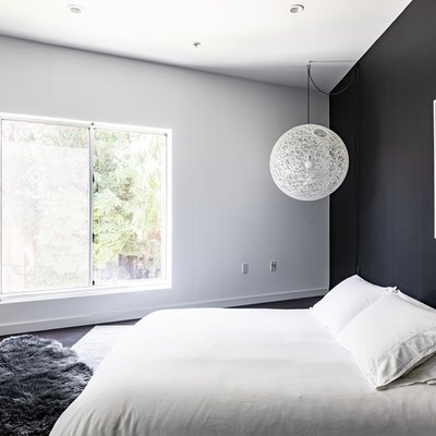 Minimalist bedroom with a black accent wall, string globe pendant light, gray fur rug, and photo art