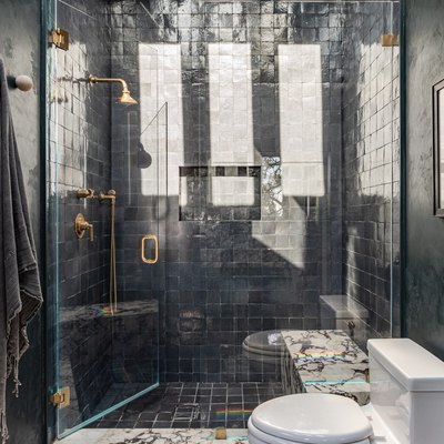 Glass door shower with square tiling and gold shower fixtures, in a dark gray walled bathroom.