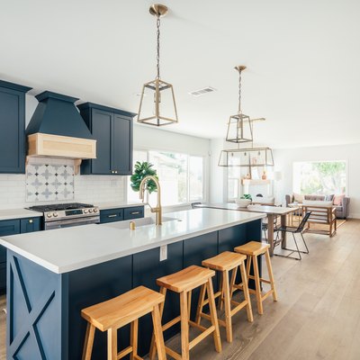 Kitchen with dark blue cabinets, kitchen island with wood stools, and gold lantern pendant lights