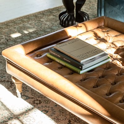 Tufted leather coffee table with books, and a claw foot side table.
