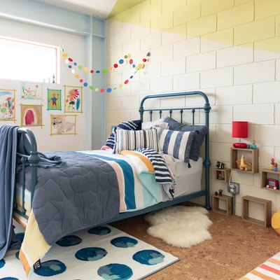 Kid's bedroom corner with yellow walls, blue bedding, primary color banner, and watercolor circle rug