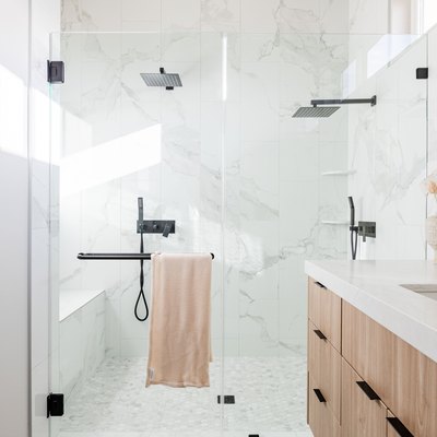 Minimalist bathroom with glass door shower, rain shower heads, and wood cabinet vanity.