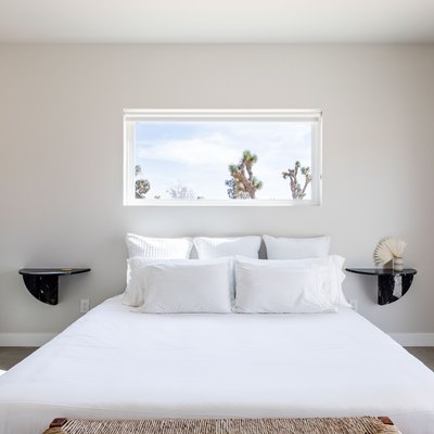 Minimalist bedroom with double black nightstand shelves, white bedding, and a desert window view.