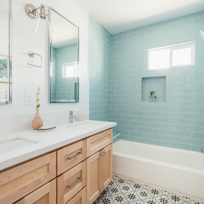 Bathroom with retro floral tile on floor, light blue subway wall tile in shower, light wood cabinet vanity with double sinks
