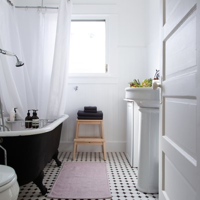 the walls, shower curtain, and most fixtures in this bathroom are white; the floor is black and white tile, and the tub stark black