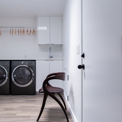 Modernist wood chair in a Minimalist laundry room with white cabinets, and a black washer and dryer.