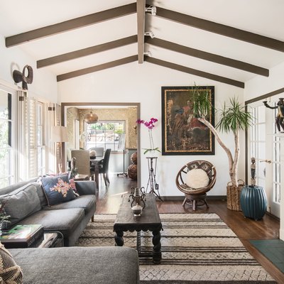 Wood beam ceiling living room with eclectic decor, gray sofa, flowers, wood coffee table, and wood-beige striped rug.