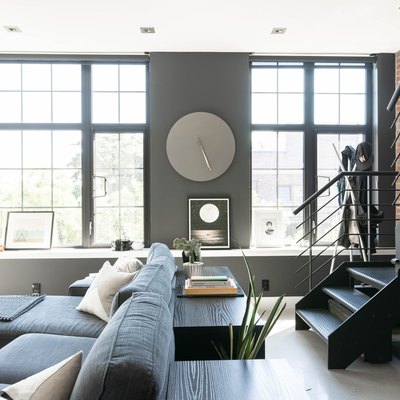 Modern upstairs living space with brick wall, grey couch with white pillows, full-length windows, couch, and long wood table