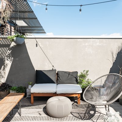 Outdoor contemporary patio with canopy, wood benches with pillows, silver metal chairs, and dried bamboo fence
