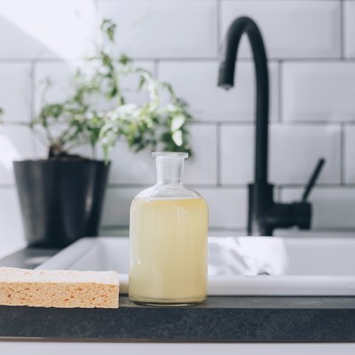 a glass bottle full of diy dish soap on a kitchen counter near the sink