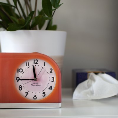 An orange retro style clock on a white desk with a plant