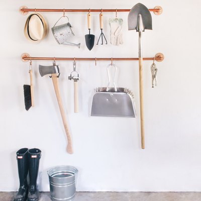 garage tools hanging on s-hooks that are suspended from copper pipes mounted on a wall