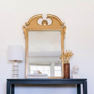 Gold antique style mirror on side table with lamp, vase of dried flowers and sculpture bust