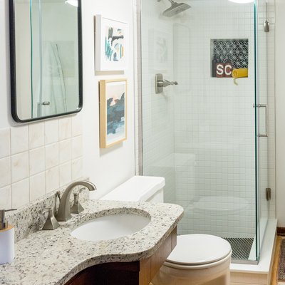 Bathroom with white wall tiles, granite vanity counter, hardwood floor, and glass door shower