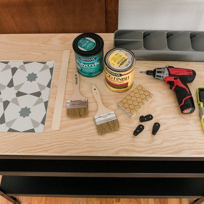 Peel-and-stick tile, paint brushes, bucket of stain, power drill, sanding block, drill bits