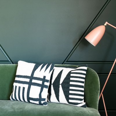 color scheme with a medium-green couch against a dark green wall next to a pink floor lamp